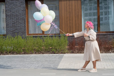 Woman holding balloons on footpath