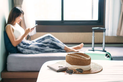 Full length of woman using mobile phone wile sitting on bed at home