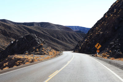 Road by mountains against clear sky during winter