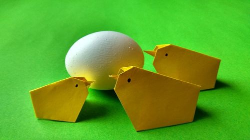 Close up of egg by yellow origami birds over green background