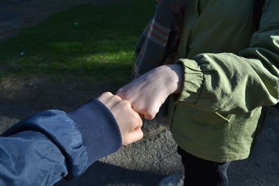 Midsection of friends fist bumping on footpath during sunny day