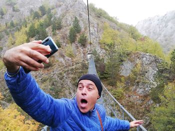 Man taking selfie from mobile phone on footbridge over mountain