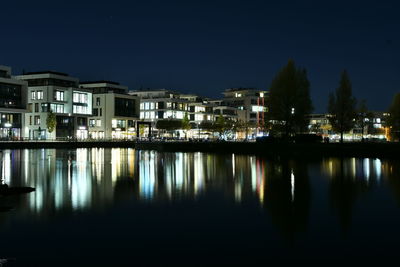 Illuminated buildings by lake against sky in city at night