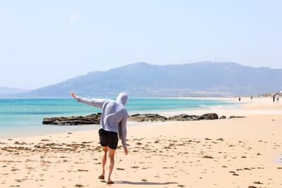 Rear view of man standing on beach against clear sky