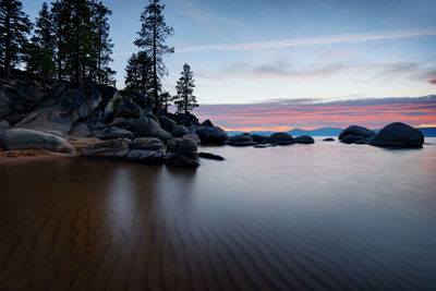 Rocks by sea against sky during sunset