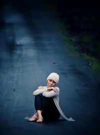 Full length of thoughtful mature woman looking away while sitting on road