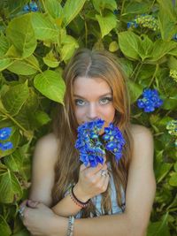 Portrait of woman with blue flowers standing by plants