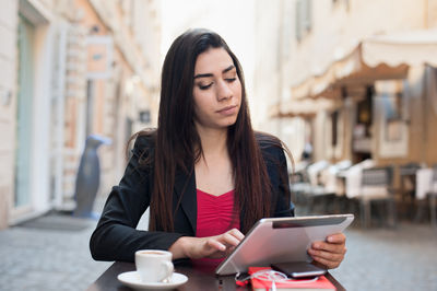 Confident businesswoman using digital tablet at sidewalk cafe in city