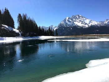 Frozen lake by snowcapped mountains against sky