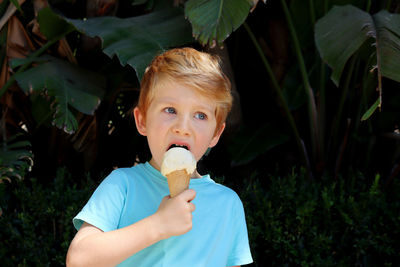  a thoughtful five-year-old boy eats sweets against a backdrop of dark green tropical leaves