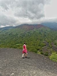 Rear view of woman walking on cliff in front of mountains