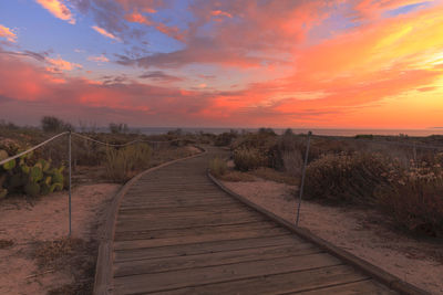 Boardwalk on beach against sky during sunset