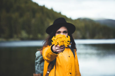 Close up view of female backpacker with hat and yellow jacket handing wild flowers