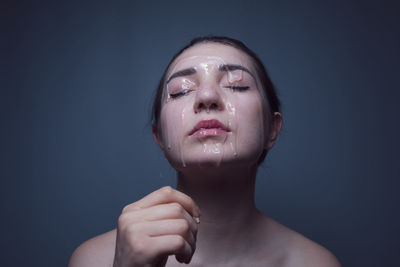 Close-up of shirtless young woman with beauty product on face against gray background