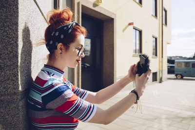 Young female hipster taking selfie while standing against wall