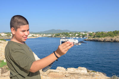 Closeup, happy teenage boy, preparing for drone flight sunny day with the sea in the background