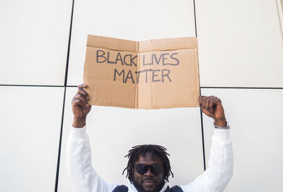 Male african american social justice warrior in sunglasses raising cardboard placard with black lives matter inscription during manifestation