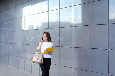 Young businesswoman talking on mobile phone while standing by wall