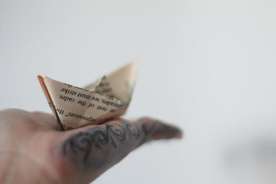 Close-up of hand holding paper boat against sky