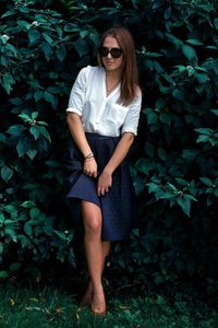 Portrait of beautiful woman wearing sunglasses standing by plants at park