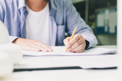 Midsection of woman holding paper while sitting on table