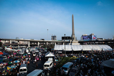 People walking on busy city street by victory monument against sky