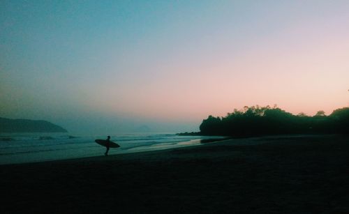 Silhouette man on beach against clear sky during sunset