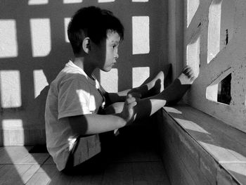 Side view of boy sitting against wall