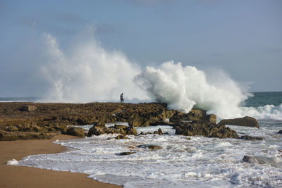 Waves splashing on rocks at shore against sky