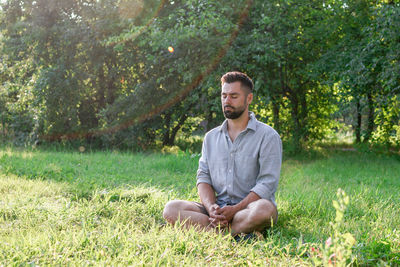 Portrait of young handsome european man in casual clothing sitting on a grass in summer park.