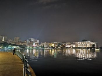 Illuminated city by sea against sky at night