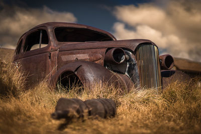 Abandoned vintage car on field against sky