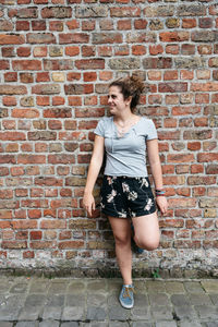 Smiling woman looking away while leaning on brick wall