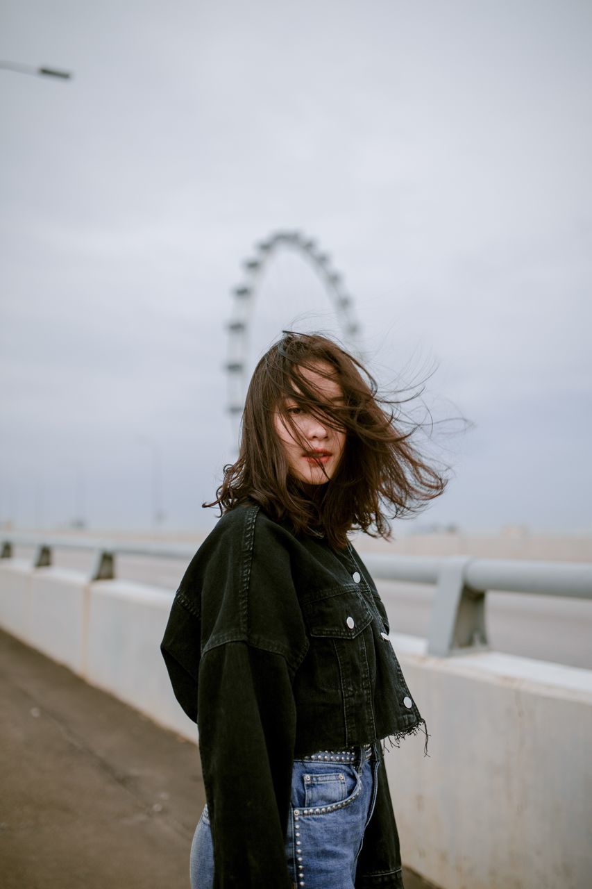 one person, standing, lifestyles, leisure activity, sky, focus on foreground, real people, casual clothing, waist up, young adult, hairstyle, three quarter length, hair, nature, long hair, brown hair, young women, women, warm clothing, tousled hair, wind, beautiful woman