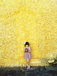 Full length of girl standing on a yellow wall