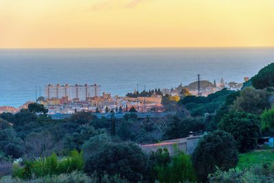 High angle view of buildings and sea against sky at sunset