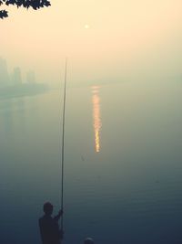 Silhouette man fishing in sea against clear sky