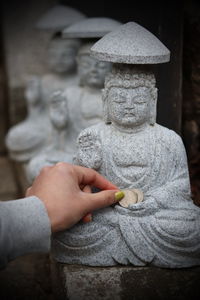 Cropped hand of woman putting money on buddha statue