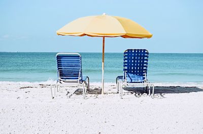 Empty lounge chairs by parasols at beach against sky