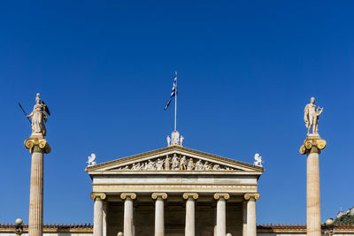 Low angle view of government building and sculptures against clear blue sky