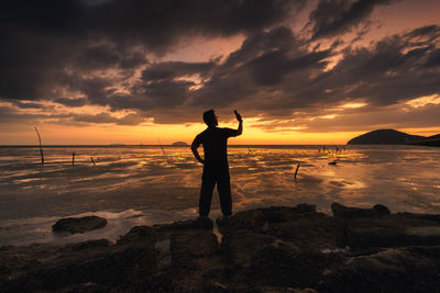 Silhouette man standing on beach against sky during sunset