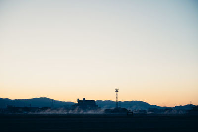 Silhouette factory against clear sky at sunset