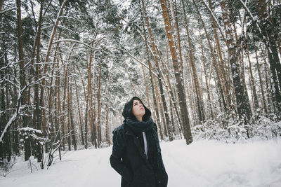 Young woman looking up while standing on snow covered field