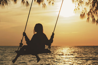 Silhouette woman swinging against sea during sunset