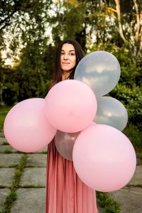 Portrait of woman with pink balloons standing against trees