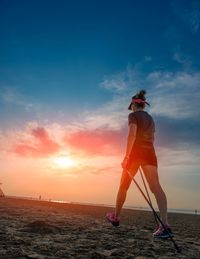 Rear view of woman standing on beach against sky during sunset