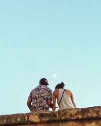 Rear view of couple sitting against clear sky