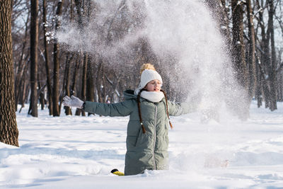 A girl in glasses and in warm clothes plays with snow in a winter park. walks in the air.