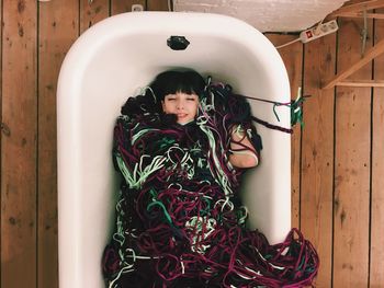 Directly above view of woman lying with yarn in bathtub on hardwood floor
