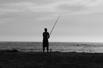 Men fishing in front of sea against sky